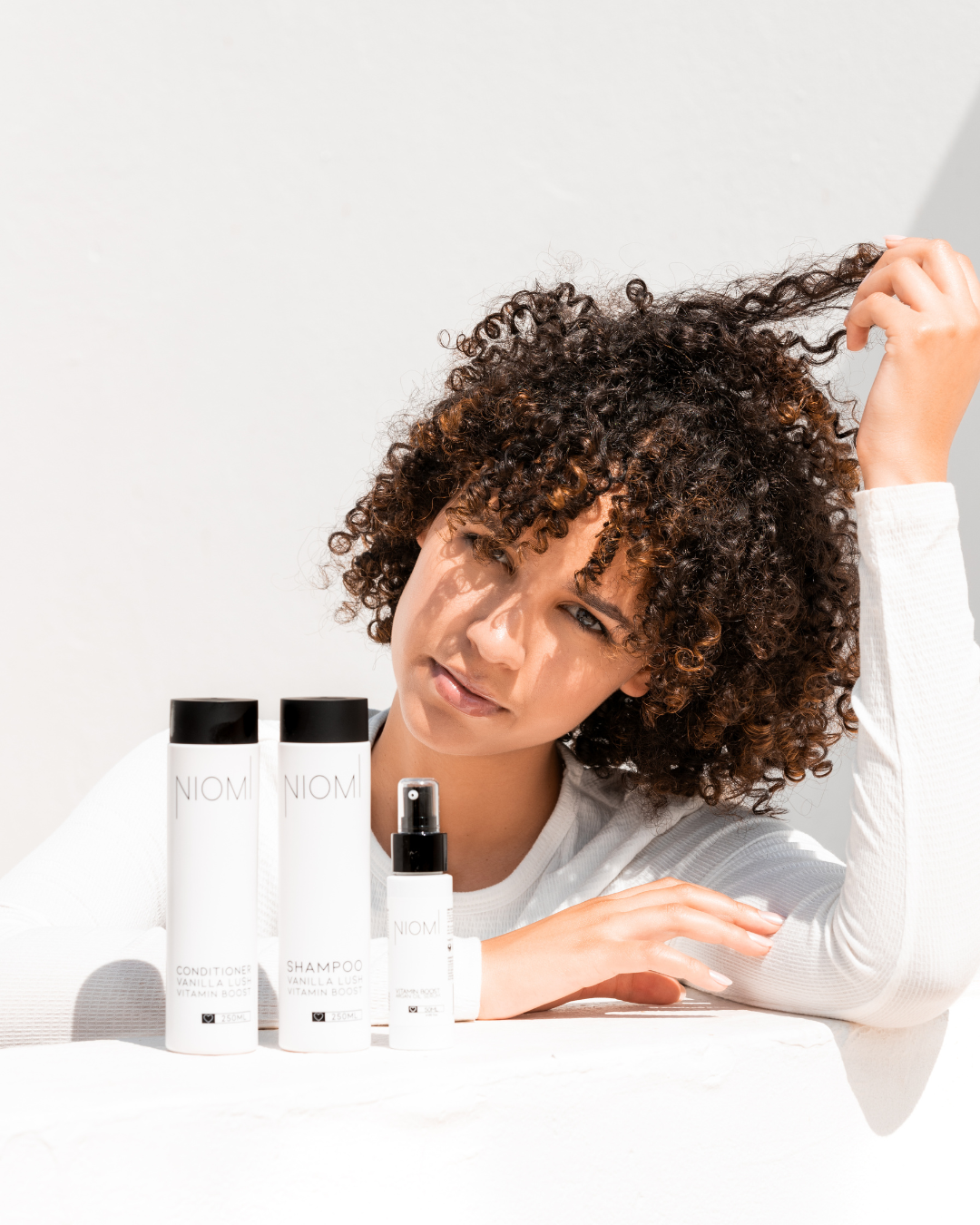 Woman with curly hair interacting with NIOMI hair care products on a white background