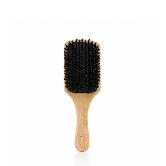 A NIOMI paddle hairbrush with a light natural bamboo handle and black bristles, shown against a plain white background.