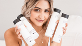 A woman holds four NIOMI haircare bottles including shampoo and conditioner, against a clean white background.