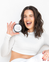 A woman with wavy brown hair is smiling and laughing while holding NIOMi Fibre Paste