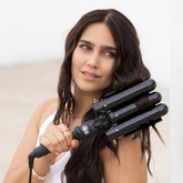 A woman with long, wavy dark brown hair holds a NIOMI 32mm Wave Wand