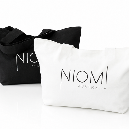Two canvas tote bags on a white background, one black with white printed text and one white with black printed text. The white bag is in front and clearly shows the brand name 'NIOML AUSTRALIA'.